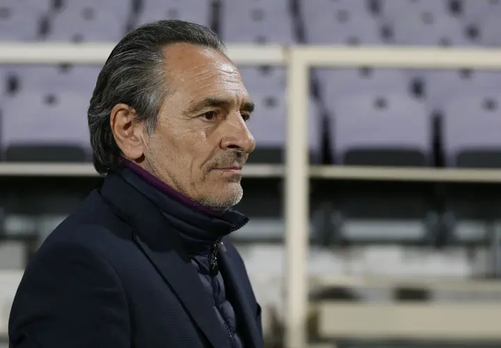 Prandelli, zamyślony trener, w ciemnej kurtce i marynarce, z fioletowym kołnierzem, na tle pustych trybun.