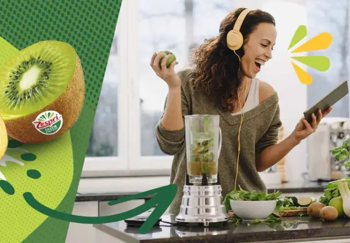 Glad kvinna med hörlurar gör smoothie med kiwi nyttigt. Två halverade kiwifrukter syns till vänster.
