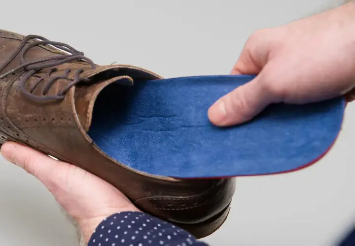 Braune Lederschuhe mit blauen Innenschuhen. Eine Hand hält die Einlage, die andere den Schuh.