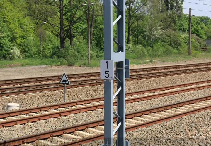Słup z tabliczką 15-16,4, czyli hektometr kolejowy, obok torów kolejowych.