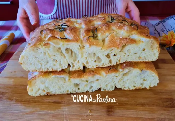 Focaccia alta e soffice, tagliata a metà, con rosmarino e sale grosso. La mollica alveolata promette un sapore delizioso.