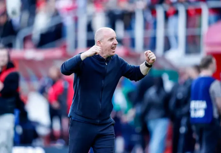 Nowy trener Widzewa, z zaciśniętymi pięściami, krzyczy z radości na tle trybun.