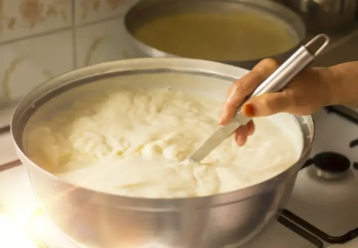 Mano che mescola un pentolone pieno di cremoso yogurt da bere fatto in casa, pronto per essere gustato.