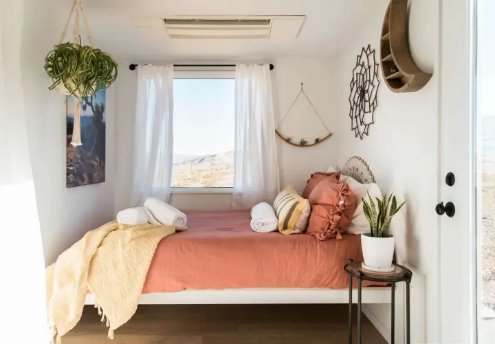 Cozy small bedroom layout with a bed, window view, hanging plants, and desert-inspired decor.
