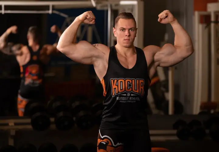 Mężczyzna w koszulce sportowej prezentuje umięśnione ramiona, inspirując do tego, jak zwiększyć masę mięśniową.