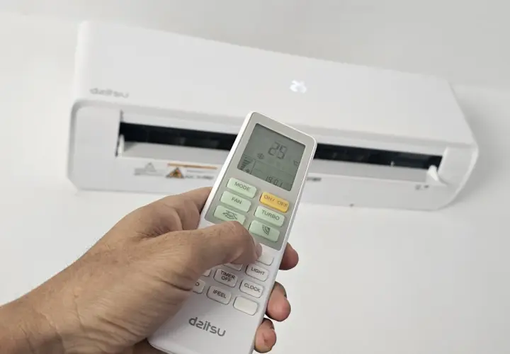Mano ajustando el control remoto de un aire acondicionado Daitsu. Para poner el aire acondicionado en invierno, selecciona el modo "Calor" o "Heat" en el control.