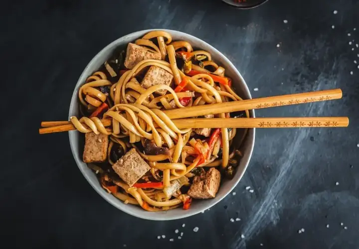 Miseczka pełna makaronu udon z tofu i warzywami, gotowa do jedzenia. Idealny makaron udon przepis na szybki obiad.