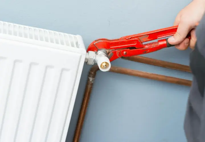 Un idraulico usa una chiave per regolare il raccordo di un termosifone bianco, mostrando come si misura interasse termosifoni per un'installazione corretta.