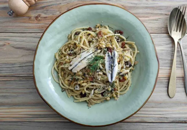 Assiette de pâtes au poisson italienne, garnie d'anchois, de pignons de pin et de raisins secs.