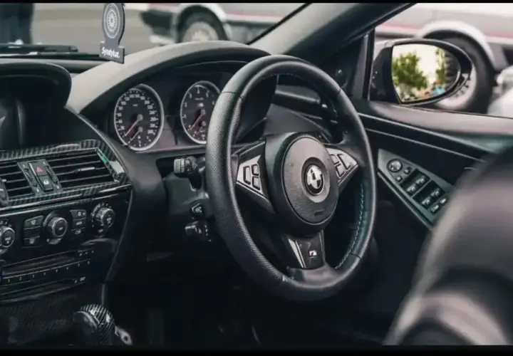 Wnętrze BMW E64 z czarną kierownicą, deską rozdzielczą i karbonowymi wstawkami.