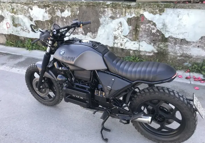 Moto BMW customizzata in stile cafe racer, con serbatoio grigio opaco, sella nera e borse moto laterali in pelle.