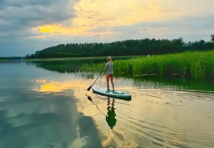 Kobieta na desce SUP, ciesząca się zachodem słońca nad jeziorem. Idealny czas na relaks, może nawet w okolicach Bożego Ciała.