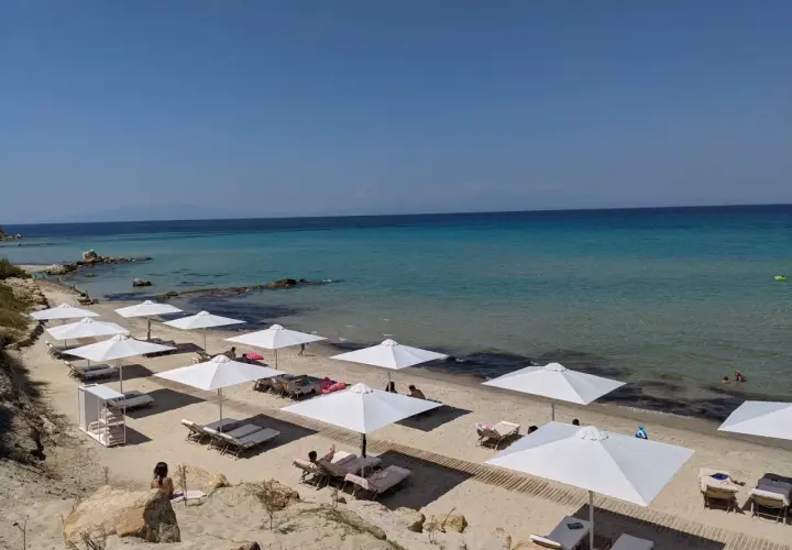 Traumhafter Karibik-Strand auf Chalkidiki mit weißen Sonnenschirmen und Liegen am türkisfarbenen Meer.