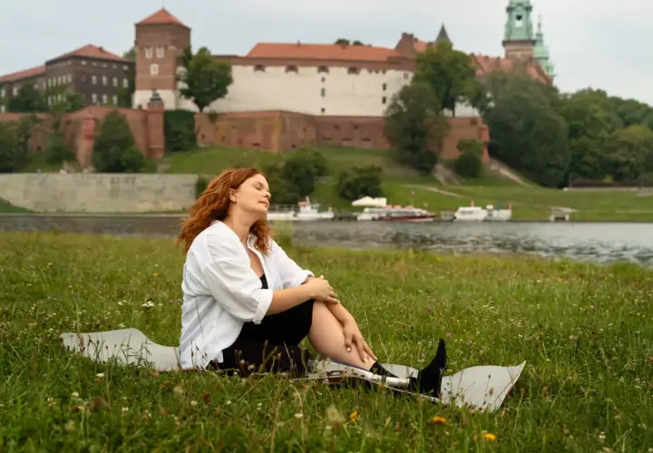Kobieta z rudymi włosami odpoczywa na trawie z widokiem na Wawel. Idealne miejsce na jednodniowe wycieczki z Krakowa.