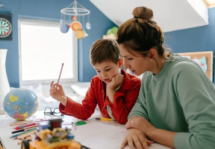 Mama z synem uczą się w domu. Czy edukacja domowa jest płatna? Na biurku globus, kredki i książki.