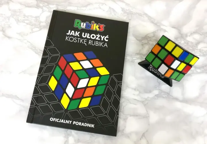 Książka "Jak ułożyć kostkę Rubika" i kostka Rubika na podstawce.