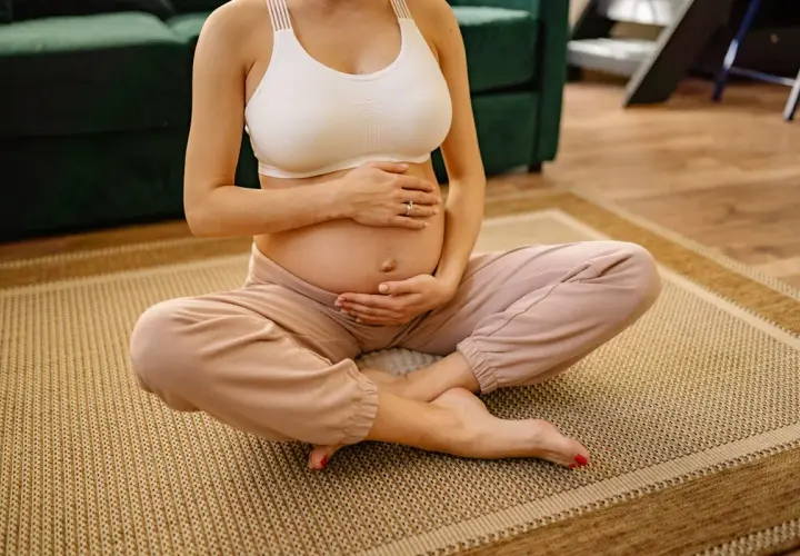 Donna incinta seduta a gambe incrociate sul tappeto, mani sull'addome. Si percepiscono i movimenti del feto a diverse altezze.