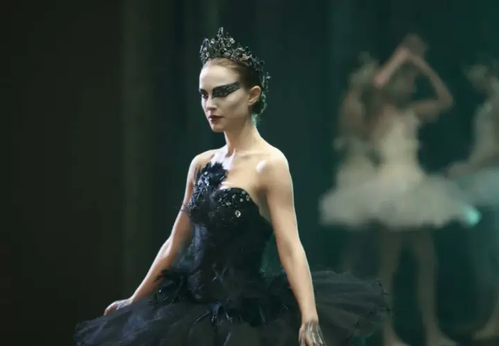 Natalie Portman jako Czarny Łabędź w koronie i czarnej tutu, z innymi tancerkami w tle.