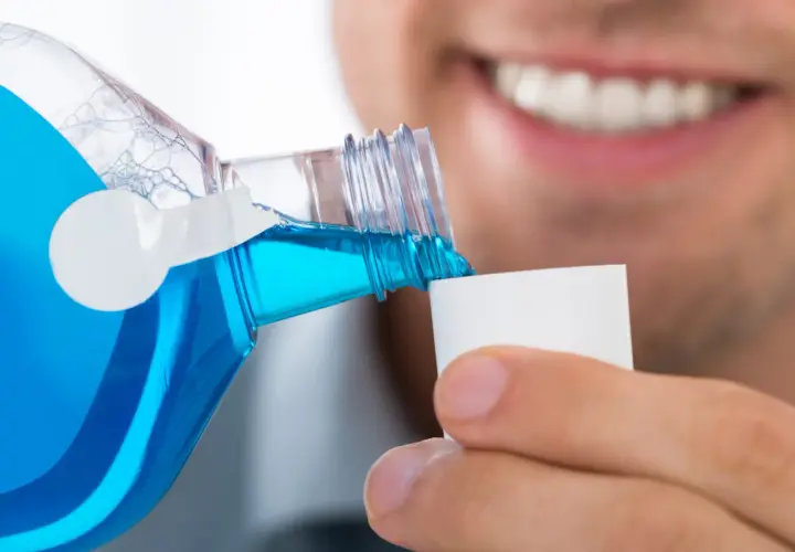 Un uomo versa colluttorio blu in un tappo, un gesto di cura dopo l'estrazione di un dente.