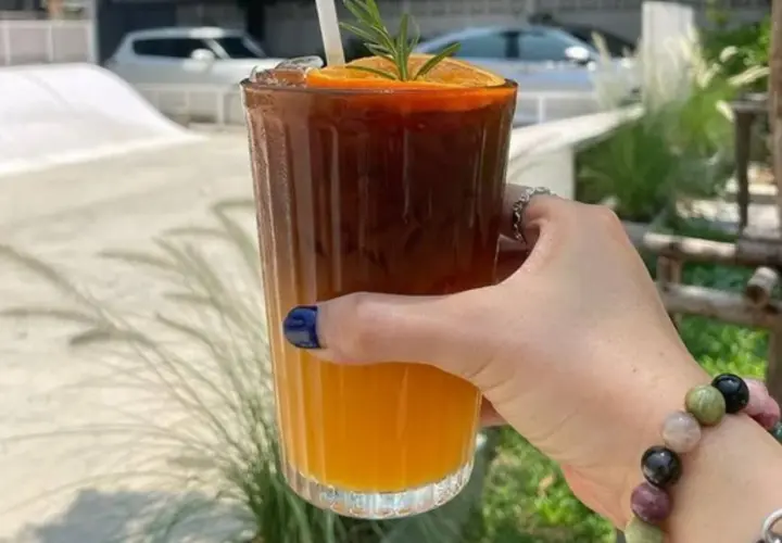 Orzeźwiające espresso z sokiem pomarańczowym, ozdobione plasterkiem pomarańczy i gałązką rozmarynu, w dłoni z kolorową bransoletką.