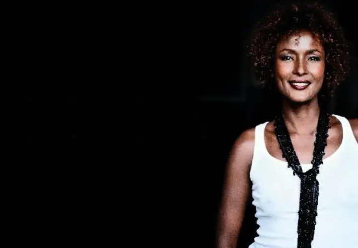 Waris Dirie w białej koszulce i czarnym naszyjniku, uśmiecha się.