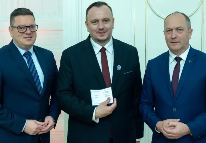 Trzech mężczyzn w garniturach. Środkowy, zasłużony dla kolejnictwa, trzyma certyfikat.