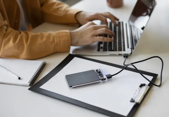 Un homme tape sur son ordinateur portable, un disque SSD externe est branché.