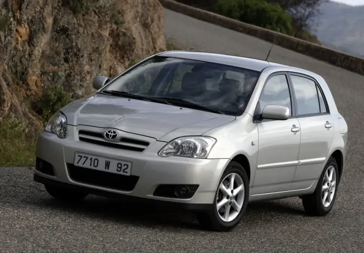 Srebrna Toyota Corolla E12 hatchback na krętej drodze wśród skał i zieleni.