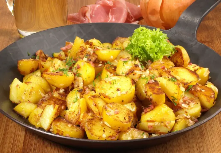 Goldbraune Bratkartoffeln mit Speck und Zwiebeln, garniert mit Petersilie. Ein klassisches Bratkartoffeln Rezept, serviert in einer Eisenpfanne.