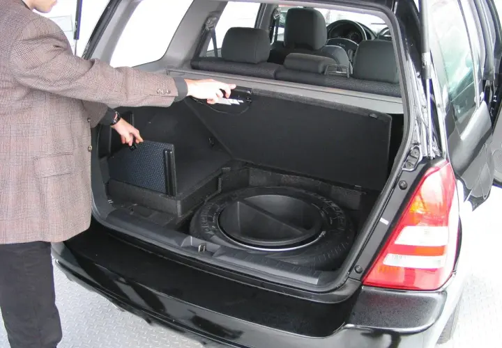 Mężczyzna otwiera bagażnik, pokazując schowek na koło zapasowe i subwoofer. Awaryjne otwieranie bagażnika może być konieczne w razie problemów.