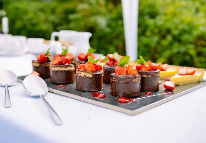Catering przerwa kawowa: czekoladowe mini torty z truskawkami i cytrynowa tarta na eleganckim talerzu.