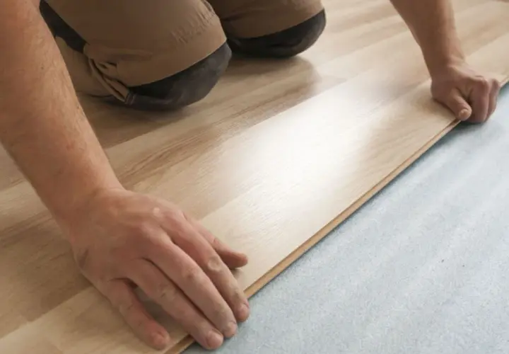 Mani esperte posano un nuovo pavimento in laminato chiaro su un sottofondo grigio. Si può posare gres su parquet, ma questo è un altro tipo di installazione.