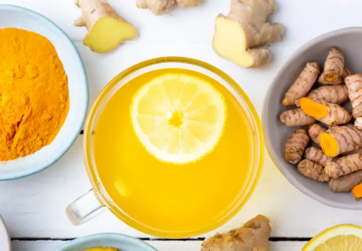 Tazza di bevanda gialla con limone, curcuma in polvere e radici, un potente antinfiammatorio naturale per intestino.