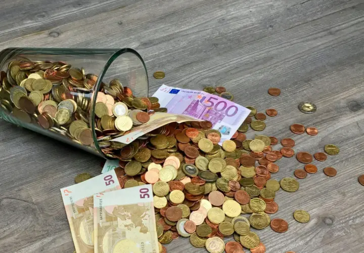 Słoik z monetami i banknotami, w tym 500 euro, rozsypany na drewnianej podłodze. To waluta Francji i innych krajów strefy euro.