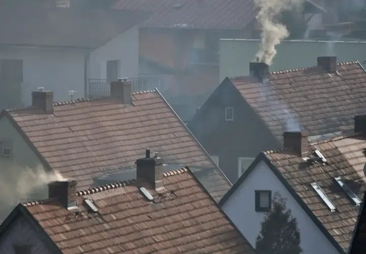 Dym wydobywający się z kominów domów na tle osiedla.