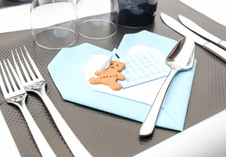 Un biscuit en forme d'ours sur une serviette bleue, prêt pour un baptême. Le tableau budget baptême est bien organisé.