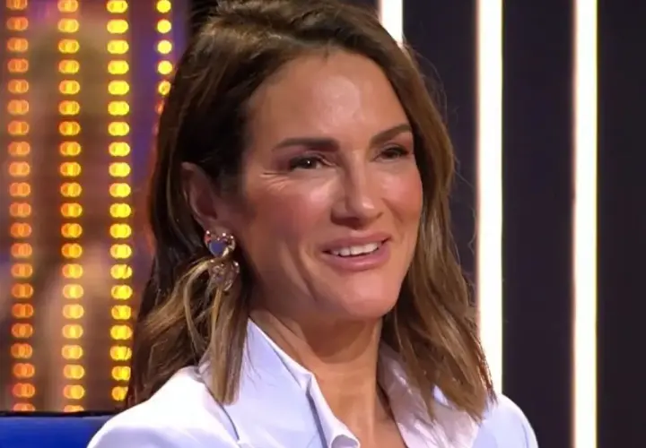 Elena, madre de Adara, sonríe con pendientes de corazón. Fondo de luces.