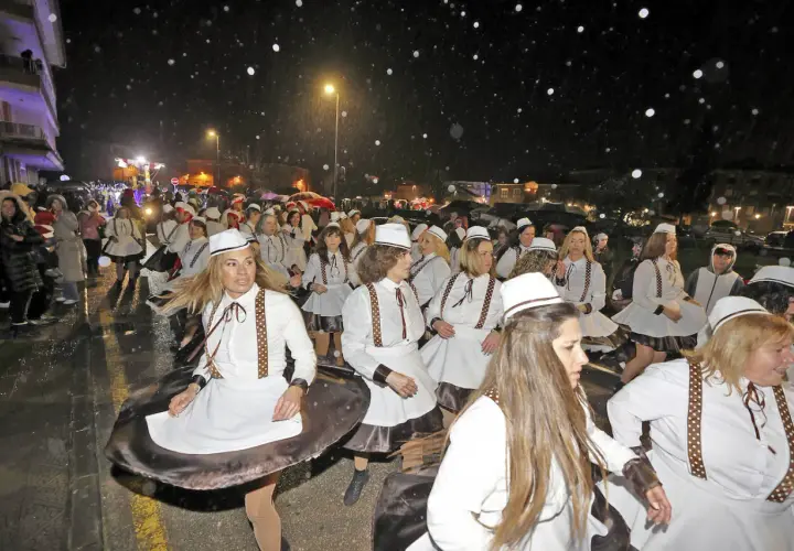 Desfile de mujeres con trajes blancos y sombreros en el carnaval cabezon de la sal, bajo una noche lluviosa.