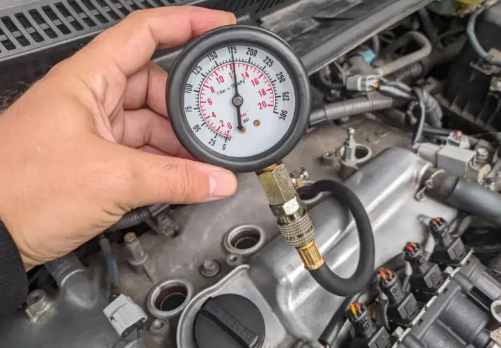 Mężczyzna sprawdza kompresję silnika za pomocą manometru. Wskaźnik pokazuje ok. 170 psi.