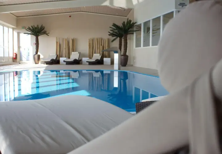 Relaks przy basenie w hotelu Radisson Blu Cottbus. Leżaki czekają na gości obok błękitnej wody i palm.