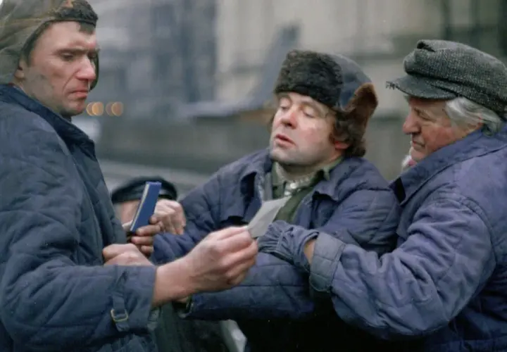 Trzech mężczyzn w zimowych kurtkach i czapkach, w tym jedna z futrzanymi uszami, dyskutuje, trzymając w rękach dokumenty. Scena z filmu "Miś" z niezapomnianą obsadą.