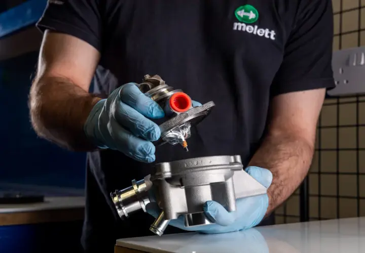 Mano con guante azul sostiene un turbo y su carcasa, inspeccionando posible perdida de aceite por el turbo.