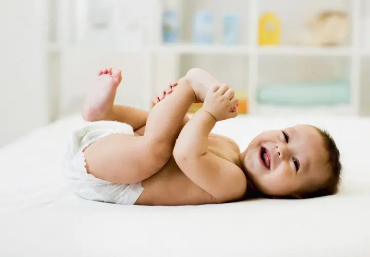 Bambino sorridente in pannolino gioca con i piedini, felice dopo aver fatto la cacca neonato.