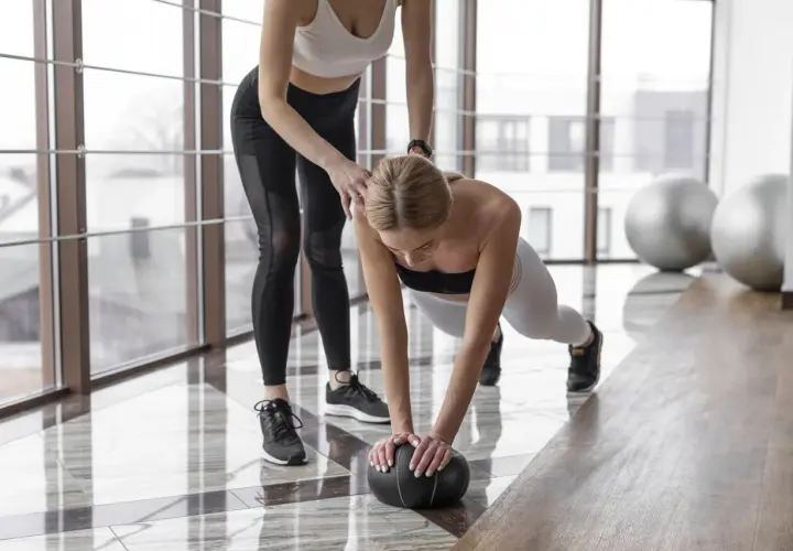 Trenerka pomaga w ćwiczeniu pompki z piłką. Zastanawiasz się, ile cardio w tygodniu jest optymalne?