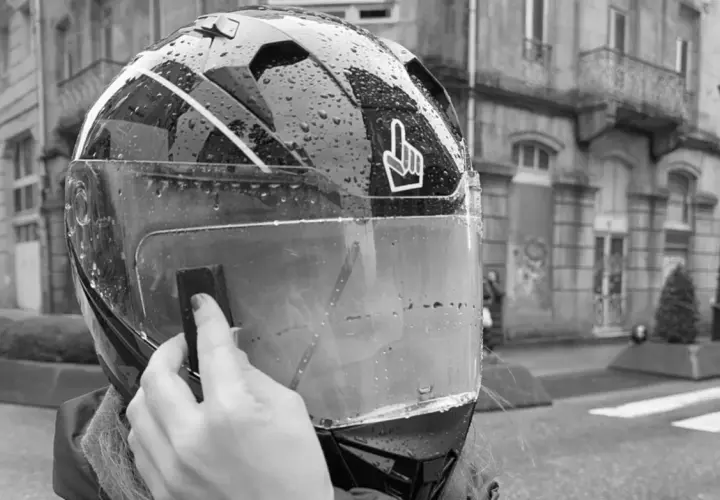 Mano colocando el Pinlock en un casco de moto mojado por la lluvia, listo para instalar.