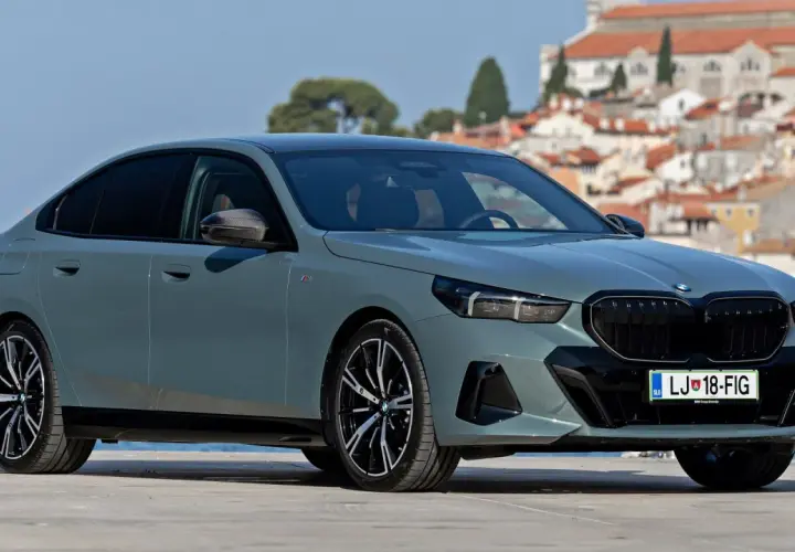 Eleganckie, szare BMW 520 z czarnymi felgami stoi na tle malowniczego, nadmorskiego miasteczka.