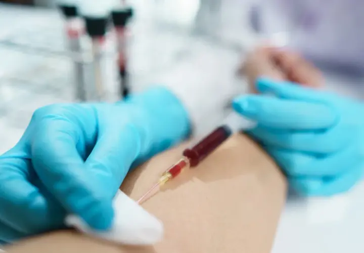 Felczer pobiera krew do strzykawki z żyły pacjenta, przygotowując próbkę do analizy.