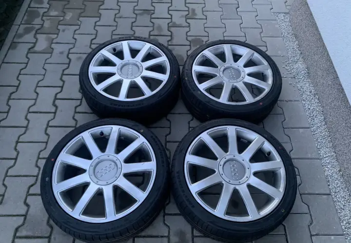 Cztery felgi aluminiowe z oponami do Audi A2. Rozmiar opon widoczny na jednej z nich to 205/55 R16.