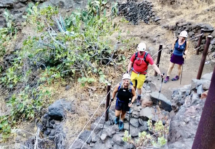 Wanderer steigen die felsige Masca Schlucht hinauf. Sie tragen Helme und Wanderstöcke.