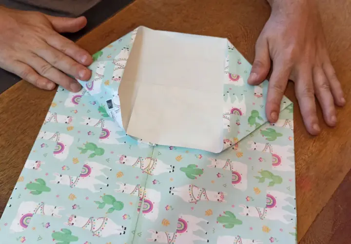 Mani che piegano carta regalo con lama e cactus per creare mini sacchetti di carta fai da te.